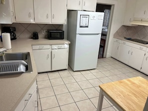 Compact kitchen with a refrigerator, microwave, and sink under a window.