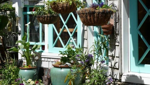 Una casa con porche, decorado con macetas colgantes y diferentes plantas.