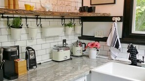 Una cocina con armarios blancos, encimera de mármol, plantas colgantes y una cafetera.