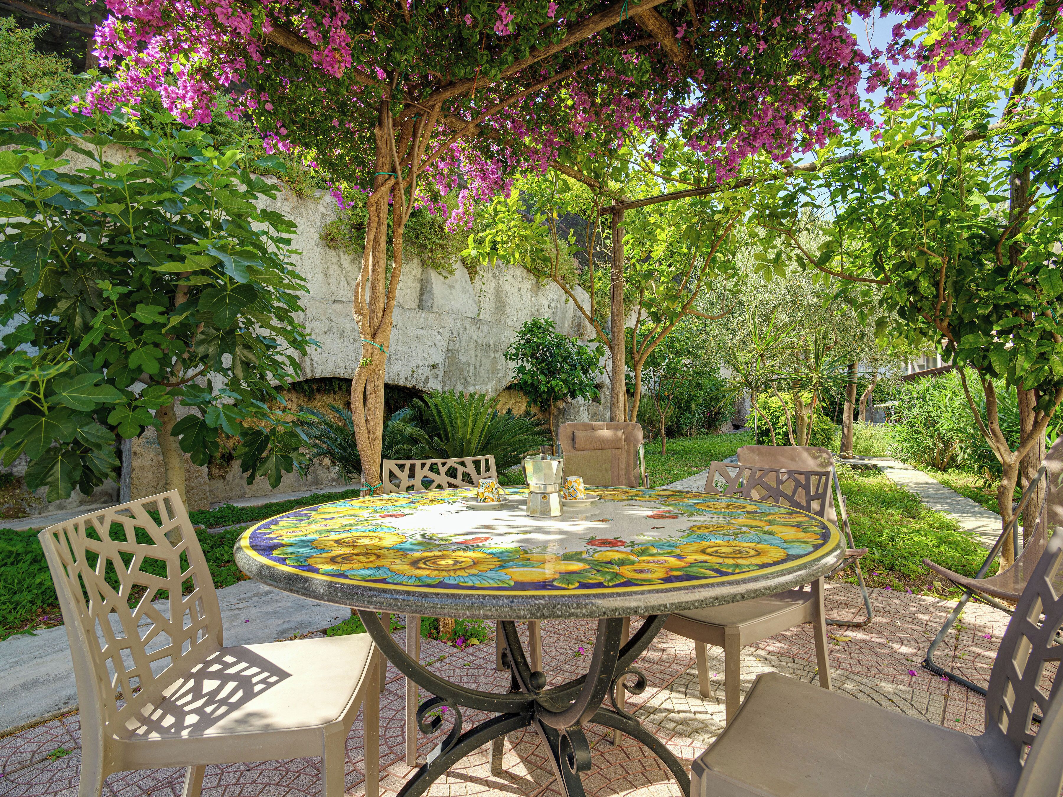 Une terrasse extérieure avec une table ronde, des chaises et une pergola couverte de plantes grimpantes fleuries.