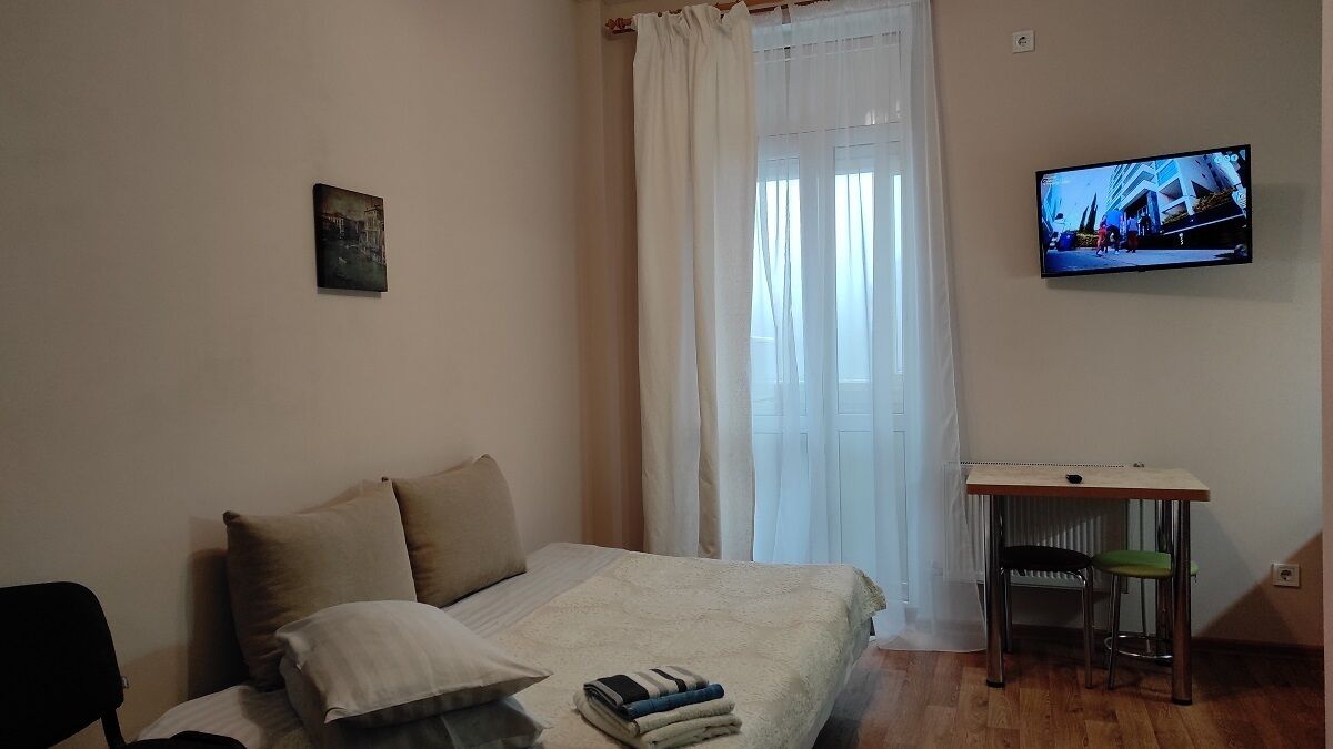 A bedroom with a bed, a TV, a small table, and a window with curtains.