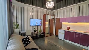 A modern living room with a sofa, TV, and a kitchen area with a counter and cabinets. - Apartments Levada  (Kharkiv)