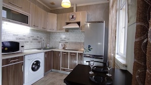 A modern kitchen with wooden cabinets, a built-in microwave, a washing machine, and a dining area with a table set for two. - Apartments Levada  (Kharkiv)