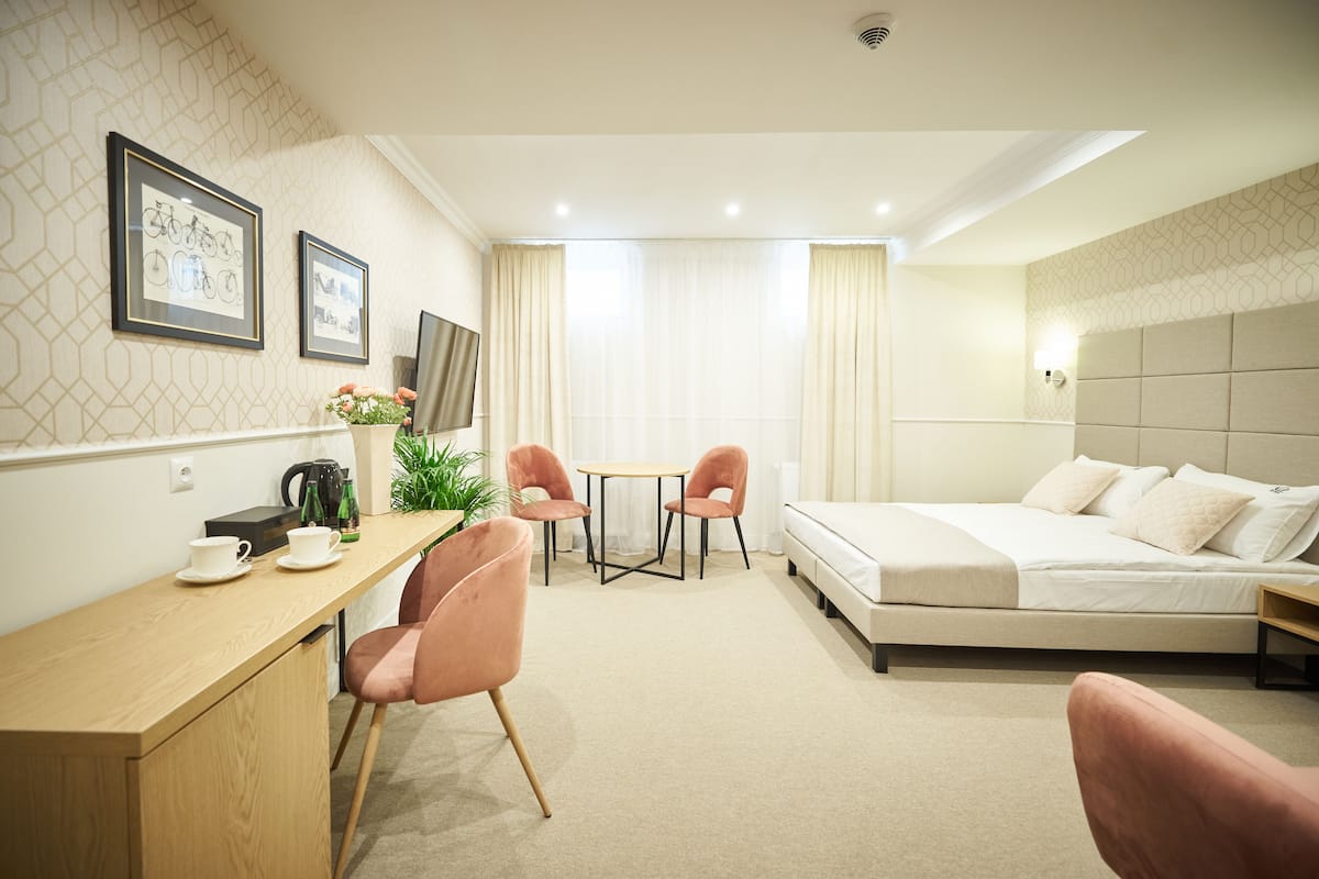A hotel room with a bed, a desk with a chair, a television, and a window with curtains.