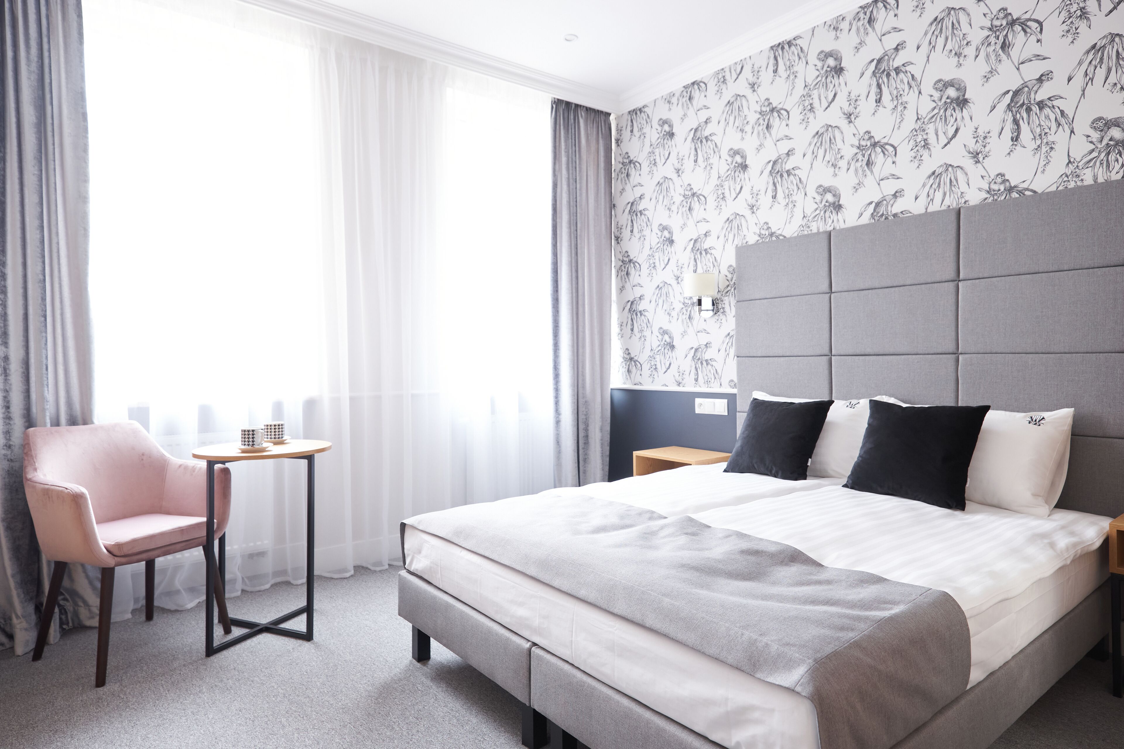 Une chambre d’hôtel avec un grand lit, une petite table, une chaise et une vue sur l’extérieur à travers des rideaux légers.