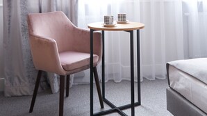Una habitación con una cama, una silla, una mesita con dos tazas y un ventanal con cortinas traslúcidas.