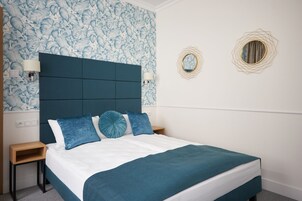 A bedroom with a large bed, a headboard, two bedside tables, and a wall with a floral pattern.