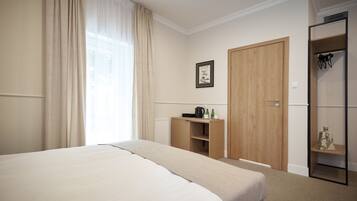 A hotel room with a large bed, a wooden wardrobe, a radiator, and a shelf with items.