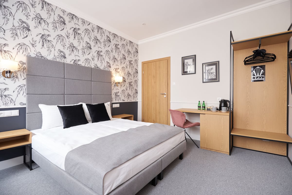 A modern hotel room with a large bed, a desk, and a wardrobe.