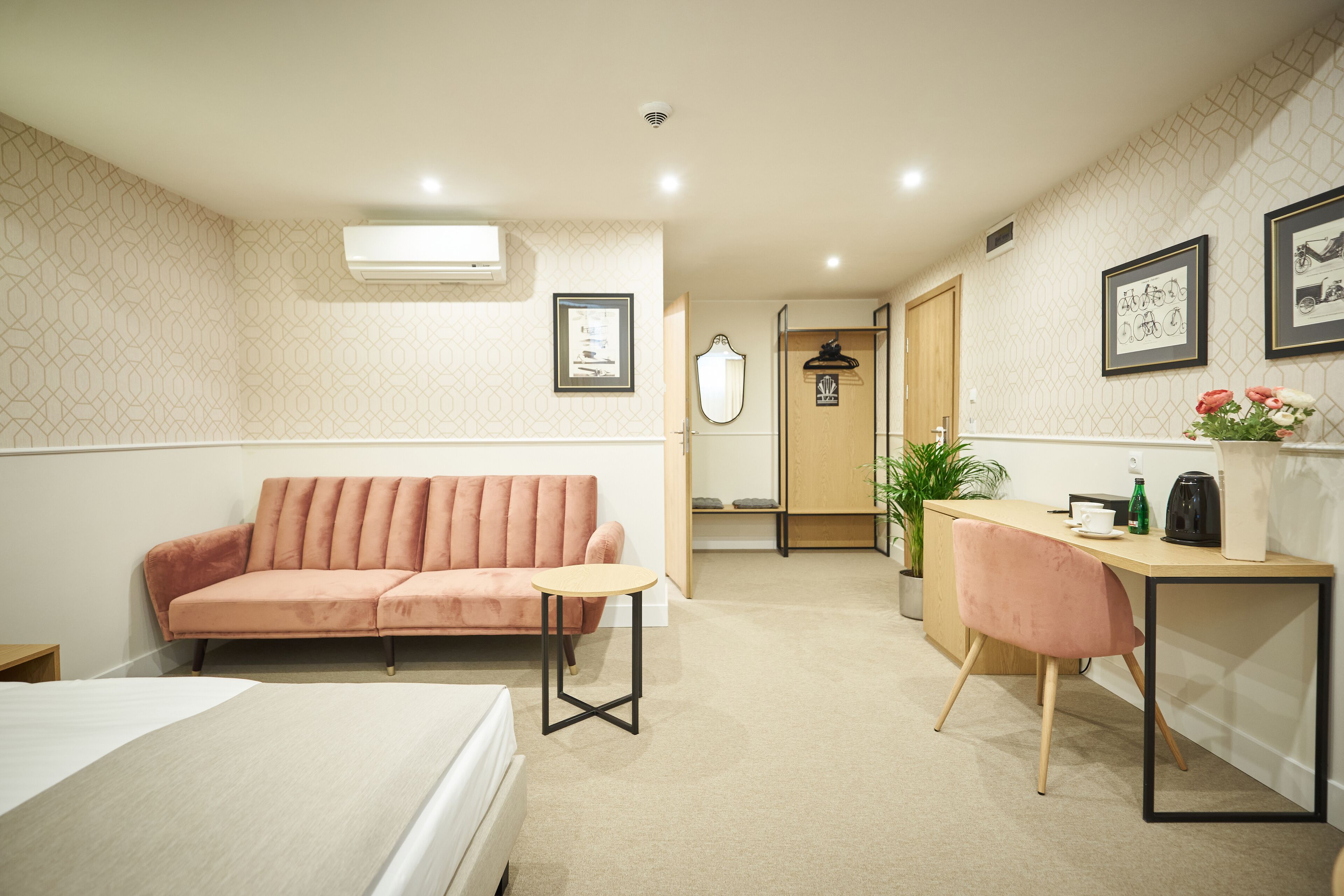 A compact hotel room with a bed, a sofa, a desk, and a small table.