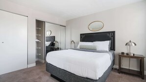 A modern bedroom with a large bed, a bedside table with a lamp, a wardrobe, and a mirror on the wall. - Walk to Nightlife & Attractions (Indianapolis)