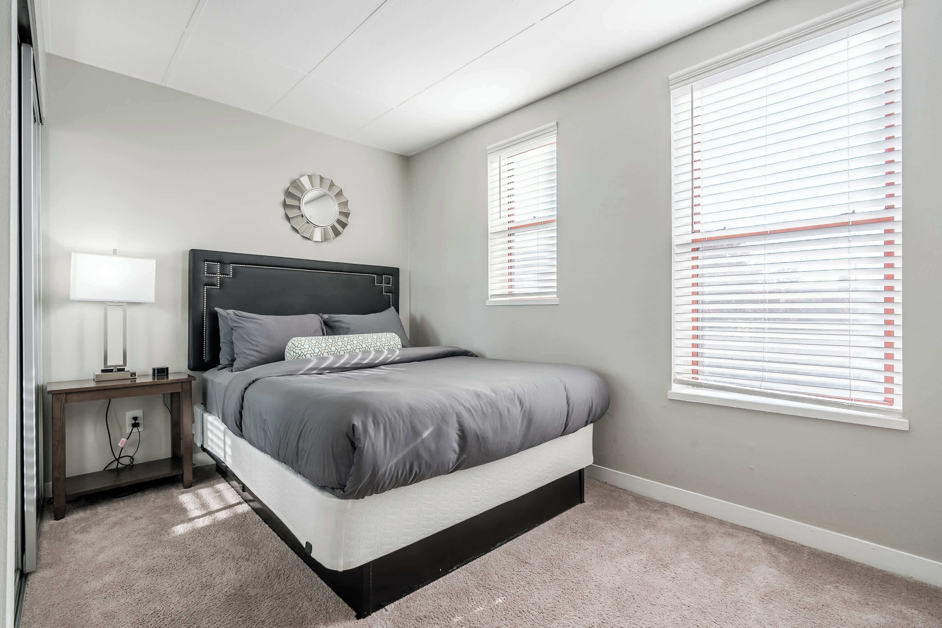 A bedroom with a bed, bedside table, lamp, and a wall clock.
