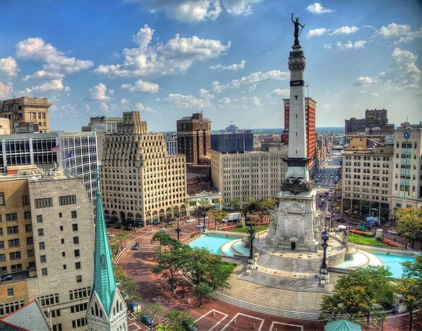 A cityscape with a prominent monument in the center, surrounded by a circular plaza with a fountain.