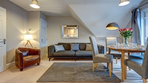 Una sala moderna con un sofá, sillones, una mesa de centro y una mesa de comedor preparada para cuatro comensales.