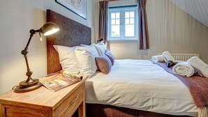 Una cama bien hecha con sábanas blancas, una mesita de noche de madera con una lámpara y una ventana con cortinas.