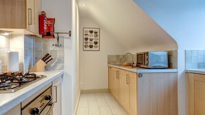 Una cocina con estufa a gas, microondas, armarios de madera y extintor.