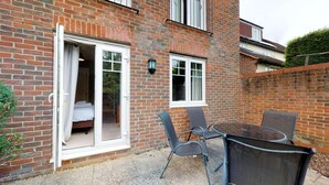 A brick house with a sliding glass door leading to a bedroom. There is a small patio with a table and chairs.