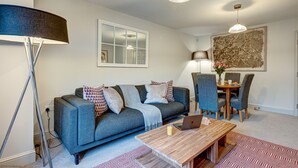 A living room with a sofa, a coffee table, a dining table with chairs, a lamp, and a painting on the wall.