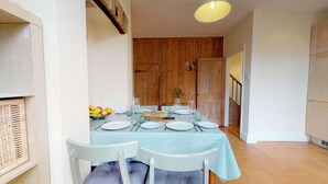 A dining area with a table set for four, surrounded by white chairs, with a wooden door in the background. - Abbey Road | Oxford Holiday Let | 2 Beds & Sleeps 3 (Oxford)
