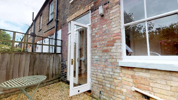 A brick house with a wooden fence, a metal table, and a white door. - Abbey Road | Oxford Holiday Let | 2 Beds & Sleeps 3 (Oxford)