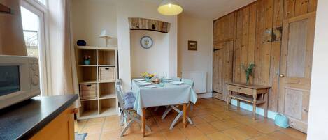 Una cocina con una mesa de comedor para dos personas, un microondas, una estantería con cestas y una puerta de madera.