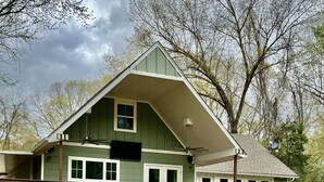 A two-story building with a green exterior, a balcony with outdoor seating, and a staircase leading to the upper floor. - Top Location! 3D & Video Tour. Riverside 4/3 w/ the best water access & privacy! (Flippin)