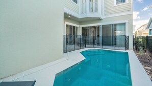 Een zwembad met terrasoverkapping en een woonhuis met grote ramen en een balkon, met vrij uitzicht op het zwembad.