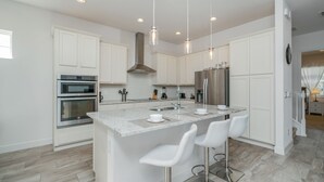 Een moderne keuken met witte kasten, roestvrijstalen apparatuur en een centraal eiland met barstoelen.