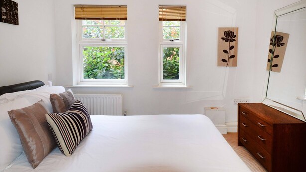 Ein Schlafzimmer mit einem Bett, zwei Fenstern, einer Kommode und einem Spiegel.