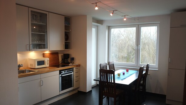 A modern kitchen with white cabinets, a microwave, and a dining table with chairs. - Nice, centrally located apartments in Cologne, streetcar stop in front of the door. (Köln)