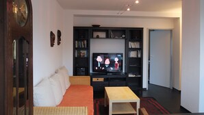 A living room with a television, a sofa, a wooden coffee table, and built-in bookshelves. - Nice, centrally located apartments in Cologne, streetcar stop in front of the door. (Köln)
