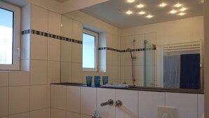 A bathroom with white tiled walls, a white sink, a mirror, and a glass shower enclosure. - Nice, centrally located apartments in Cologne, streetcar stop in front of the door. (Köln)