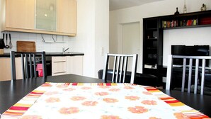 A modern kitchen with white cabinets, a black countertop, and a dining table with a floral tablecloth. - Nice, centrally located apartments in Cologne, streetcar stop in front of the door. (Köln)