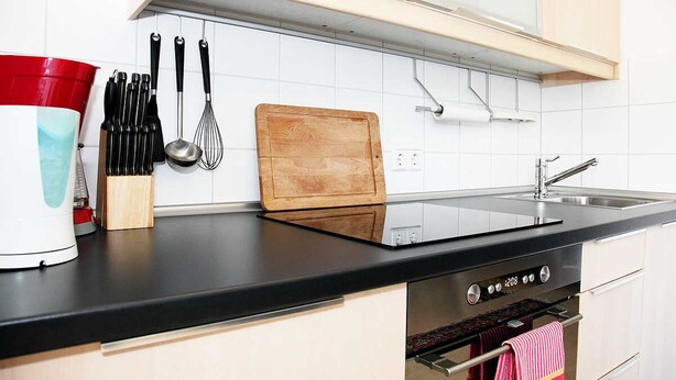 A kitchen with a black countertop, white tiles, a wooden cutting board, and a red and white appliance. - Nice, centrally located apartments in Cologne, streetcar stop in front of the door. (Köln)