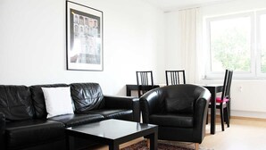 A modern living room with a black leather sofa, a coffee table, and a dining area with chairs. - Nice, centrally located apartments in Cologne, streetcar stop in front of the door. (Köln)
