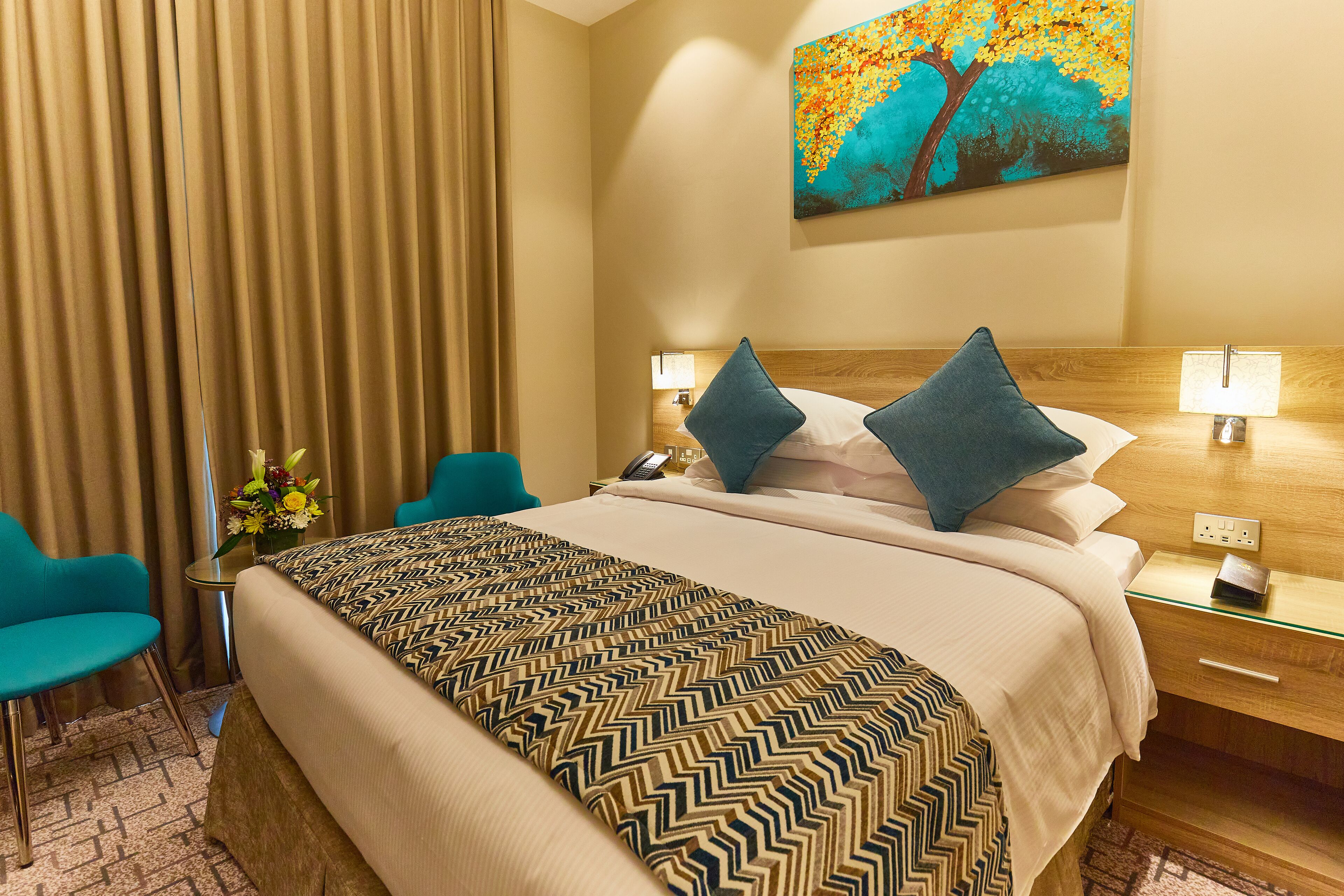 Een hotelkamer met een groot bed, twee kussens, een nachtkastje met een lamp, een stoel en een schilderij aan de muur.