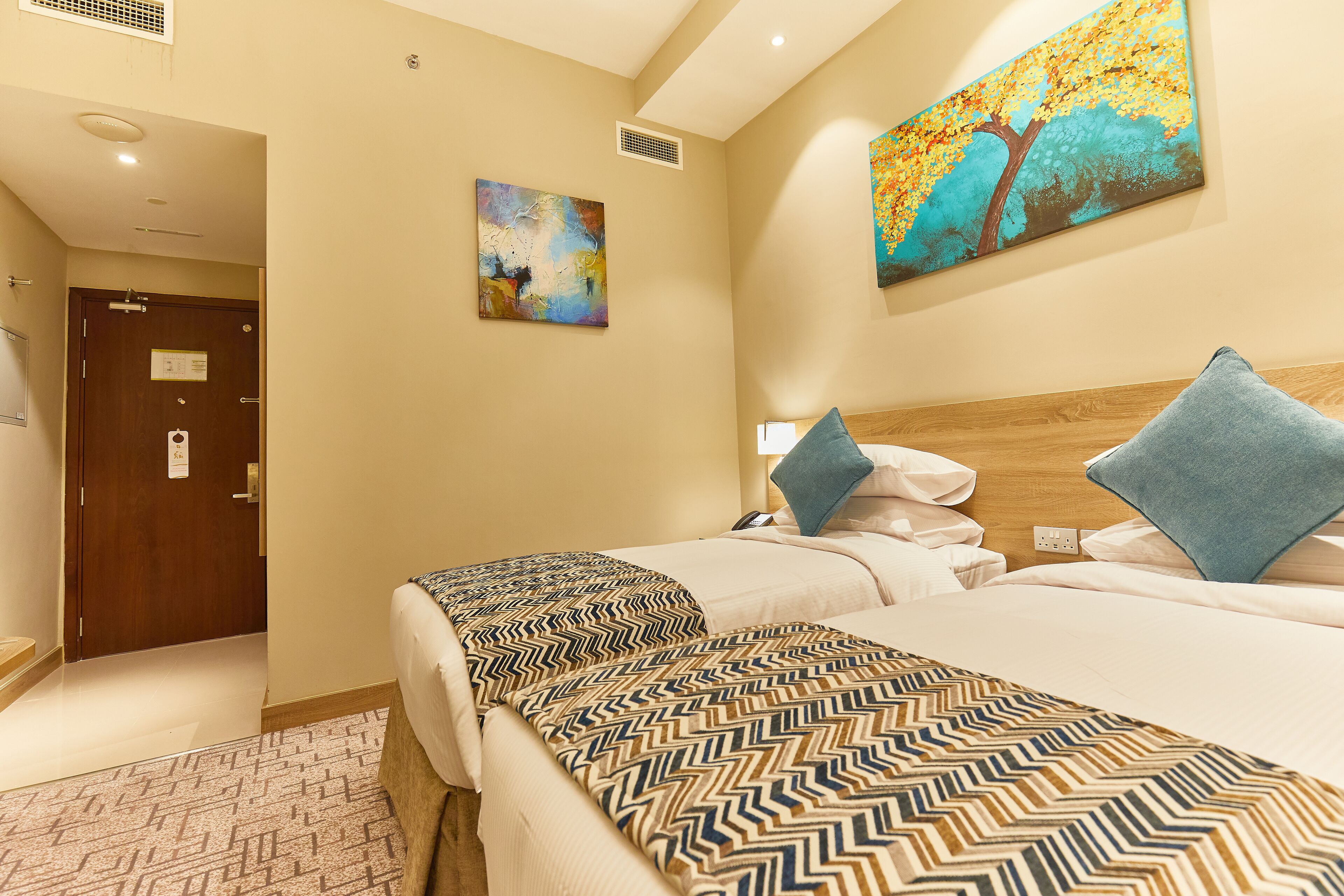 Une chambre d’hôtel avec deux lits, une tête de lit en bois, une couvre-lit à motifs et deux tableaux accrochés aux murs.