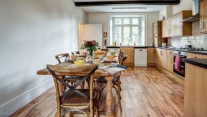 A kitchen with wooden flooring, a dining table with chairs, and a window with a view of greenery. - The Bladon Farmhouse | Oxfordshire Holiday Let | 2 Beds & Sleeps 5 (Bladon)