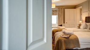 A hotel room with two beds, a large window with curtains, and a door leading to another room. - The Bladon Farmhouse | Oxfordshire Holiday Let | 2 Beds & Sleeps 5 (Bladon)