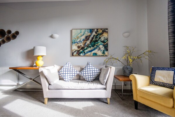 A modern living room with a sofa, a yellow armchair, a coffee table, and a painting on the wall. - The Beauchamp Suite Dunara 4 | Leamington Spa Holiday Let | 1 Bed & Sleeps 2 (Leamington Spa)