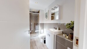 Ein modernes Badezimmer mit einer Duschkabine, einer weißen Toilette und einem Waschtisch mit Spiegel und Waschbecken.
