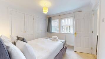 A bedroom with a bed, two doors, a window with blinds, and a ceiling light.