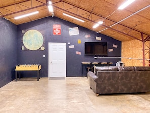 A room with a dark blue wall, a white door, a large flat-screen TV, a leather couch, a foosball table, and various signs on the wall.