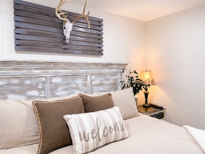 A bedroom with a wooden headboard, a bed with beige bedding, and a welcome pillow.
