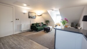 A modern apartment with a green sofa, a small table, and a kitchen area.