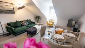 A cozy living room with a green sofa, a yellow armchair, and a dining table set for two.