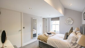 A bedroom with a bed, bedside table, mirror, and a window with a view.