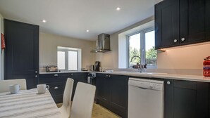 A modern kitchen with dark cabinetry, a dishwasher, and a window providing natural light. - Rose Cottage | Adderbury Holiday Let | 2 Beds & Sleeps 3 (Adderbury)