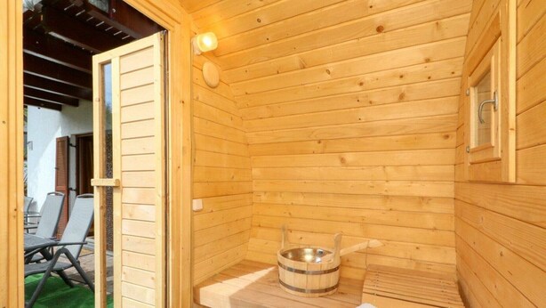 Una sauna de madera con un banco, una toalla y un recipiente metálico.