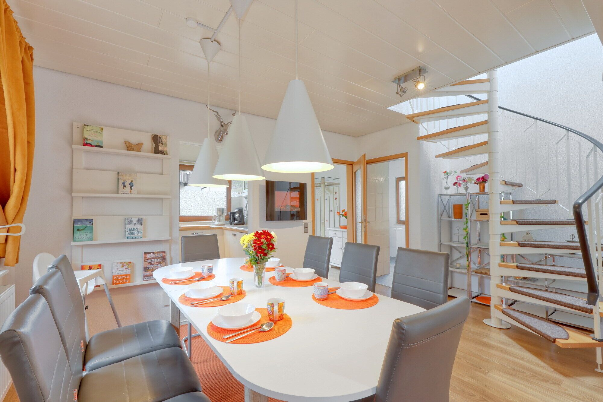 A modern dining area with a white table set for four, surrounded by grey chairs. A staircase with wooden steps and metal railings is visible to the right.